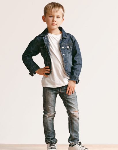 The portrait of cute little kid boy in stylish jeans clothes looking at camera against white studio wall. Kids fashion concept